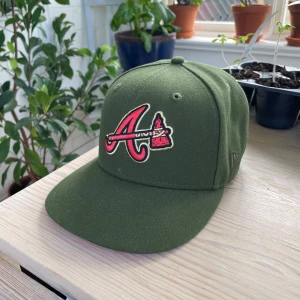 Grön Atlanta Braves keps från New Era - Snygg grön keps från New Era med Atlanta Braves-logga framtill och broderad detalj på sidan. Skärmen är röd undertill och kepsen har klassisk 59FIFTY-passform. Perfekt för dig som gillar sportiga accessoarer. Storlek 58,7