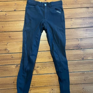 Marinblå ridbyxor från Pikeur - Marinblå ridbyxor från Pikeur med helskodd silikongrepp. Byxorna har normal passform, bälteshällor och klassisk knappstängning. Snygg Pikeur-logga på höften och stretchigt material som ger bra rörelsefrihet.