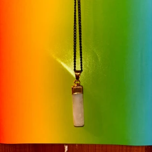 Halsband med rosenkvarts kristall - Snyggt halsband med en rosenkvarts kristall. Kedjan är tunn och svart, vilket ger en cool kontrast till kristallen och gulddetaljen. Perfekt för att lyfta vilken outfit som helst.