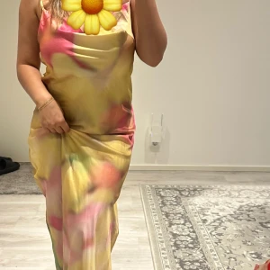 Färgglad långklänning i satin - Säljer en långklänning i satin med färgglada toner av gult, rosa och grönt. Klänningen har smala axelband och en mjukt draperad urringning. 