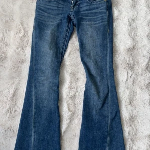 Blå bootcut jeans från True Religion - Säljer ett par klassiska blå bootcut jeans från True Religion med snygga kontrastsömmar och dekorativa fickor bak. Jeansen har gylf med dragkedja och knappar samt detaljerade ficklock med guldfärgade knappar. Storlek w23. Fint skick