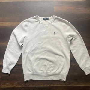 Vit sweatshirt från Polo Ralph Lauren - Klassisk vit sweatshirt från Polo Ralph Lauren med broderad logga på bröstet. Tröjan har rund halsringning och långa ärmar. Perfekt för en stilren och enkel look.