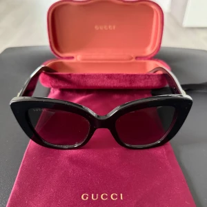 Svarta cat eye-solglasögon från Gucci - Tjenare säljer tjejens solglasögon då dom är använda väldigt fåtal gånger och eftersom dom helt enkelt bara ligger där | Ett par Snygga svarta cat eye-solglasögon från Gucci med breda skalmar och guldfärgad Gucci-logga på sidan|Kommer med originalfodral i vinröd sammet och matchande tygpåse| kan även gå ner lite i pris vid snabb affär| tveka inte på höra av er vid frågor och funderingar| Ha det bäst 🌄🤩