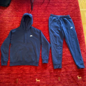 Mörkblå Nike tracksuit dress - Mörkblå hoodie från Nike med klassisk logga på bröstet. Tröjan har huva med dragsko och en stor magficka framtill. Perfekt för en avslappnad stil.