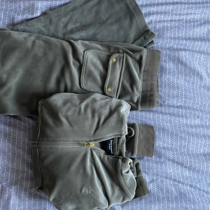 Olivgrön hoodie och mjukisbyxor från Juicy Couture - Säljer ett matchande set från Juicy Couture i olivgrönt. Hoodien har dragkedja, huva med snören och känguruficka. Byxorna har resår i midjan, snörning och fickor med lock och guldknappar bak. Helt nya har använt 3-4 gånger koftan är XL och den kom lite tajt på mig som tar på mig L så det är nice att ha den om man tar på sig storlek M-L vill man inte ha den tajt tajt då S funkar med. Byxorna är storlek L. Helt ny alltså ser inte ens använd ut.