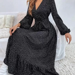 Svart långklänning med vita prickar - Snygg svart långklänning med vita prickar och v-ringad omlott-topp. Klänningen har långa ärmar med lätt puff och markerad midja. Perfekt för dig som gillar en klassisk men trendig look.