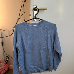 Blå stickad tröja - Mysig blå stickad tröja med rund halsringning och långa ärmar. Tröjan har ribbade muddar vid ärmslut och nederkant, perfekt för kyligare dagar. Enkel och stilren design som passar till mycket.