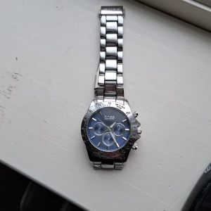 Hugo Boss Klocka - Stilren herrklocka från HUGO BOSS med länkarmband i silverfärgat metall och blå urtavla. Klockan har tre mindre urtavlor och tydliga markeringar på boetten. Perfekt accessoar för dig som gillar klassisk design.