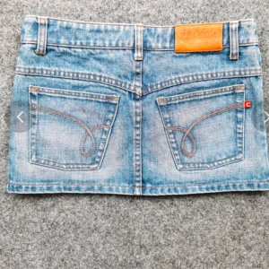 Blå jeanskjol med fickor - Säljer en klassisk blå jeanskjol med snygga bakfickor och bälteshällor. Kjolen har knapp och dragkedja framtill samt dekorativa sömmar. Perfekt för dig som gillar denim och vill ha en enkel men trendig look. Jättefin och mycket bra skick! Från one teaspoon. Skriv till mig innan ni köper!  