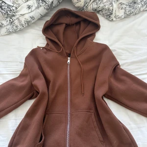 Brun koftan med dragkedja från SHEIN - Mysig brun kofta från SHEIN med dragkedja framtill och luva. Jackan har två fickor och är tillverkad i ett mjukt fleecematerial. Perfekt för kyliga dagar när du vill vara både bekväm och snygg. Använd cirka 5 gånger.