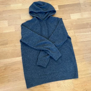 Mörkgrå merinoull hoodie - Säljer en mörkgrå stickad hoodie med huva och dragsko. Tröjan har långa ärmar och ribbade muddar vid ärmslut och nederkant. Perfekt för kyliga dagar och enkel att matcha med jeans eller andra byxor.