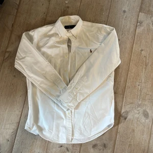 Vit Ralph lauren skjorta - Säljer en stilig vit skjorta från Ralph Lauren med broderad logotyp på bröstet. Skjortan är classy och passar perfekt som att plagg för lager på lager! Den ger en stilren look för lite special sammanhang. Den är aningen skrynklig då jag inte strykt den. Skulle passa någon mellan 180-187! Skriv om ni har några funderingar🤗