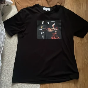 Svart t-shirt från Off-White med tryck - Säljer en svart t-shirt från Off-White med ett konstnärligt tryck på bröstet. T-shirten har rund hals och korta ärmar. Perfekt för dig som gillar streetwear och vill sticka ut med en unik design.