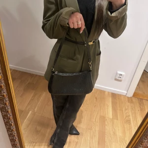 Elegant svart axelväska med krokodilpräglat - Elegant svart axelväska med krokodilpräglat mönster i läder. Silverfärgade metalldetaljer. 