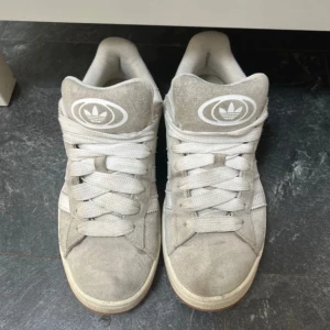 Adidas sneakers i beige mocka - Säljer ett par snygga Adidas sneakers i beige mocka med vita detaljer och klassiska tre ränder på sidan. Skorna har vit sula och breda vita skosnören. Perfekta för en avslappnad och stilren look. Köpte den för 1300 men säljer för 800 kroner. Skorn kommer komma tvättade och rena, kommer med 2 snören, vita och beiga/bruna. Inget har gått sönder kommer i hel 