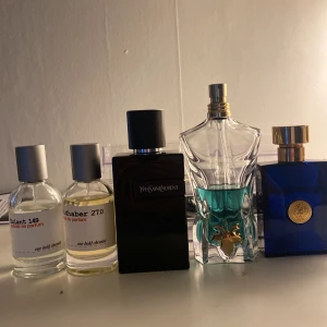 Mix av exklusiva herrparfymer - Fem  olika parfymer, Yves Saint Laurent i svart rektangulär flaska, Jean Paul Gaultier Le Male i en kroppformad flaska med blå vätska, samt Versace Dylan Blue i blå kvadratisk flaska med gulddetaljer.