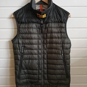 Mörk grön dunväst från Parajumpers - Säljer en mörk grön dunväst från Parajumpers, modell Daytripper. Västen har dragkedja framtill, två fickor med dragkedja och en gul detalj vid kragen. Perfekt för lager-på-lager under kyliga dagar. Får med extra knappar till den gula flärpen. Priset går alltid att diskutera!