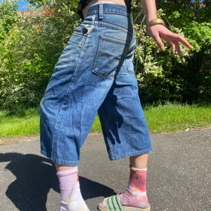 Baggy jeansshorts från Levi's - Säljer ett par blå, vida jeansshorts från Levi's med klassisk knappgylf. Shortsen har låg midja och slutar strax under knäna. Perfekta för sommardagar eller vintrar med höga sockor eller boots! Riktigt sköna och går att klä på många sätt :-)