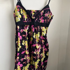 Blommig sommarklänning från H&M - Säljer en svart klänning med färgglatt blommönster i gult och rosa från H&M. Klänningen har smala axelband och v-ringning, perfekt för varma dagar. Lätt och luftig modell som ger en somrig känsla.