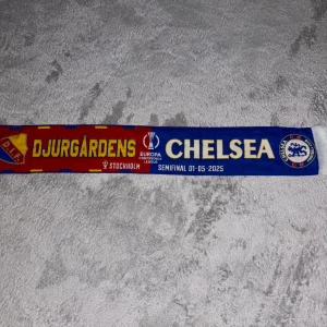 Djurgårdens IF vs Chelsea halsduk - Säljer en fotbollshalsduk med Djurgårdens IF och Chelsea från Europa Conference League semifinalen i Stockholm 2025. Halsduken har röd, gul och blå färg med klubbarnas loggor och text. Perfekt för samlare eller supportrar!