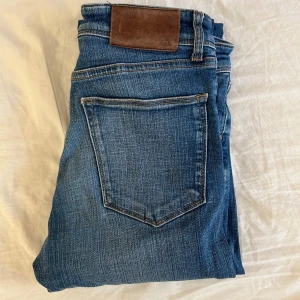 Blå jeans från J.Lindeberg - Säljer ett par klassiska blå jeans från J.Lindeberg med fem fickor och snygga kontrastsömmar. Jeansen har normal passform och raka ben, perfekt för en stilren look. Märkespatch i läder baktill i midjan. Byxorna är i strl W29/L32