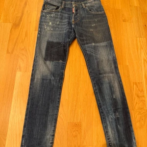 Blå jeans från Dsquared2 - Snygga blå jeans från Dsquared2 med slitna detaljer och en patch på framsidan. Klassisk femficksdesign med knappgylf och Dsquared2-logga på både fram- och baksida. Perfekta för en avslappnad stil.