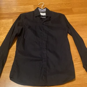 Svart slim fit-skjorta från Selected Homme – stilren & bekväm - Svart skjorta från Selected Homme i slim fit-modell. Klassisk design med lätt stretch för bekväm passform. Passar lika bra till kontoret som till festen. fint skick. Storlek: M Nypris: ca 800 Mitt pris: 200