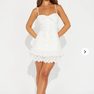 Studentklänning - Söt vit klänning med smala axelband och knytning framtill. Klänningen har spetsdetaljer och knappar längs framsidan. Perfekt för sommarens varma dagar men även för studenten om du nu behöver en utsprings klänning. Klännngen är helt oanvänd och har fortfarande prislappen kvar.