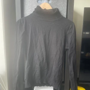 Svart polotröja - Säljer en klassisk svart polotröja med ribbad krage. Tröjan har långa ärmar och är perfekt för kyligare dagar. Enkel och stilren design som passar till det mesta.