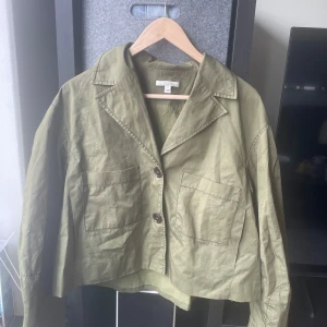  Vårjacka från Dagmar - Snygg olivgrön jacka från Dagmar med knappar framtill och två stora fickor. Jackan har en krage, är tunn och är croppad i modellen.