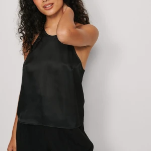 Svart ärmlös topp med spetsdetaljer - Snygg svart ärmlös topp med spetsdetaljer och korsade band i ryggen. Perfekt för en stilren look. Toppen har en elegant och enkel design som passar till många olika tillfällen.