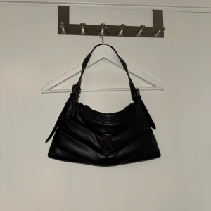 Svart axelväska med dragkedja steve madden - Snygg svart axelväska i skinn med dragkedja och dekorativa detaljer. Perfekt för att bära dina dagliga nödvändigheter med stil. Väskan har en praktisk storlek och en bekväm axelrem. Ifrån steve madden 