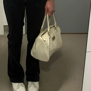 Vit quiltad handväska - Snygg vit handväska med quiltat mönster och praktiska handtag. Perfekt för att bära dina dagliga nödvändigheter med stil. Väskan har en elegant design som passar till många olika outfits.