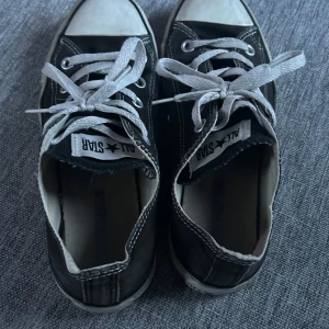 Svarta sneakers från Converse - Säljer ett par klassiska svarta Converse All Star sneakers med vita snören och tåhätta. Perfekta för en avslappnad stil. Skorna har en rund tå och är i textilmaterial. Skorna har tecken på användning men inte används mycket alls, säljer då de inte används. Hör av dig vid intresse💕