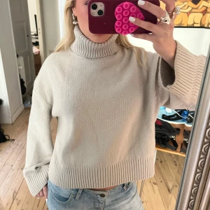 Grå polotröja - Säljer en stilren beige polotröja med ribbade detaljer vid krage, ärmslut och nederkant. Tröjan har en lös passform och långa ärmar, perfekt för kyligare dagar. Passar bra till jeans eller kjol för en avslappnad look.