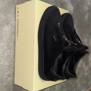 Svarta sneakers från Axel Arigato - Snygga svarta sneakers från Axel Arigato med dragkedja framtill. Skorna har en stilren design i mocka och en rund tå. Perfekta för en trendig look. Knappt använda, pris kan diskuteras, står ej för frakt men kan mötas upp i GBG