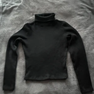 Svart ribbad polotröja - Säljer en stilren svart ribbad polotröja med långa ärmar. Perfekt för kyligare dagar och lätt att matcha med olika outfits. Ett måste i garderoben för en klassisk look. Defekter förekommer. Från Bikbok i strl 34