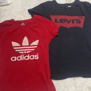  Adidas t-shirt och  Levi's t-shirt - Säljer två snygga t-shirts: en röd från Adidas med det klassiska trefoil-loggan i vitt och en svart från Levi's med röd logga. Perfekta för en casual look. Båda är kortärmade och i bekvämt bomullsmaterial.
