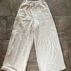 Beige mjukisbyxor från H&M  - Säljer ett par bekväma beige mjukisbyxor från H&M Divided. Byxorna har en elastisk midja och wide leg modell med avslappnad passform. Perfekta för en chill dag hemma eller en avslappnad promenad.