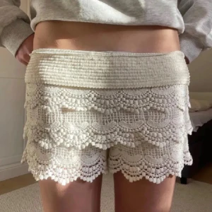 Beige spets shorts - Snygga beige shorts med vacker spetsdetalj och elastisk midja. Perfekta för en somrig look med en avslappnad känsla. De har en flerdelad spetsdesign som ger en unik och stilren touch.