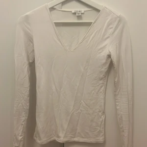 Vit långärmad topp från Amisu - Säljer en stilren vit långärmad topp från Amisu. Toppen har en v-ringad hals och är perfekt för lager-på-lager eller att bära som den är. Enkel och mångsidig design som passar till många olika outfits. Säljer den för att jag har tröttnat på den 🩷