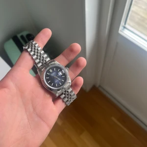Seiko automatisk klocka med blå urtavla - Säljer en elegant Seiko automatisk klocka med en djupblå urtavla och datumvisning. Klockan har en silverfärgad boett och armband i rostfritt stål. Perfekt för den som söker en stilren och tidlös accessoar. DEFEKT SOM SES PÅ BILDEN 