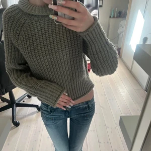 Grön stickad tröja - Säljer en mysig grå stickad tröja med en bred krage. Tröjan har långa ärmar och en något croppad passform som ger en trendig look. Perfekt för kyligare dagar!