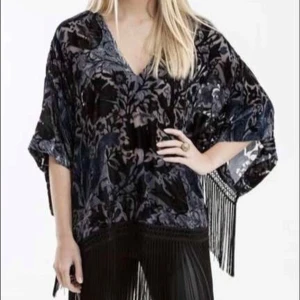 Mönstrad kimono-blus med fransar - Säljer en unik kimono-blus från Suzanne Nilsson med ett vackert blommönster i mörka nyanser. Blusen har trekvartsärmar och är dekorerad med fransar längs ärmar och nederkant. Perfekt för att ge en bohemisk touch till din outfit. Härlig kvalitet med sammets mönster i rayon (bomull) och nylon. Knappt använd. Nypris 798:-