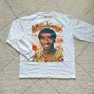 Vit långärmad minneströja - Vit långärmad tröja från RIPNDIP med minnestryck fram och bak. Tröjan har ett stort färgglatt motiv på framsidan och baksidan, med text i en dekorativ stil. Perfekt för den som vill ha ett unikt och personligt plagg.