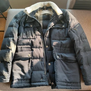 Burberry jakka  - Säljer en snygg svart quiltad jacka från Burberry med dragkedja och knappar. Jackan har en mysig krage med pälsfoder och flera praktiska fickor. Perfekt för kyliga dagar! 