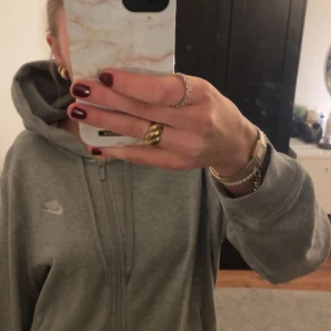 Grå hoodie från Nike - Säljer en klassisk grå hoodie från Nike med dragkedja och huva. Perfekt för en avslappnad stil. Den har en liten Nike-logga på bröstet och ribbade muddar vid ärmslut och nederkant.