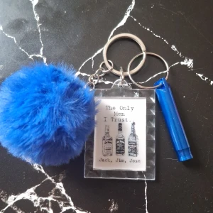 Nyckelring med blå fluffboll och citat - Säljer en nyckelring med en stor blå fluffboll och två rektangulära plattor med citat. Den ena plattan har texten 'The Only Men I Trust' med bilder av flaskor, och den andra har en illustration av en person med solglasögon och texten 'Judge Me When You Are Perfect'. Perfekt accessoar för att ge nycklarna lite personlighet. Tillsammans med en nödvisselpipa