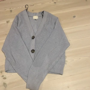 Ljusgrå/blå stickad kofta från H&M - Säljer en ljusgrå/blå stickad kofta från H&M i storlek XS. Koftan har grovstickad struktur, tre stora knappar framtill och ribbade muddar vid ärmslut och nederkant. Perfekt för hösten😍