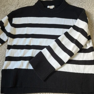 Svartvit randig stickad tröja - Säljer en svartvit stickad tröja med breda horisontella ränder. Tröjan har en ribbad högre  hals och ribbad vid ärmslut och nederkant. Skriv om ni har frågor och ska försöka posta så snabbt som möjligt.